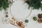 Making modern christmas wreath flat lay. Woman hands with round hoop, ribbon, candle, pine cones, golden bells on white wooden