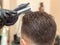 Making modern hairdo with round comb and hair dryer, close up view. Stylists hands in black rubber gloves. Males nape
