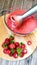 Making a ripe strawberry fruit smoothie with an electric blender. There is a cup of berry puree and whole berries on a cutting