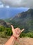 Making a Surfer hand sign with Panoramic view background of lush green foliage in Weimea Canyon and NaPali coast Kauai, Hawaii.