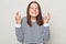 Making wish. Praying for good luck. Smiling hopeful brown haired woman wearing striped shirt posing  over gray background