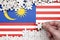 Malaysia flag is depicted on a table on which the human hand folds a puzzle of white color