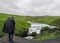 Male adult hiker adventurer hiking in raincoat back standing outdoor looking at waterfall in Laugaveur trek in stunning icelandic