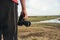 A male amateur photographer with a camera stands on a hill near a green meadow at sunset. Photorapher landscaper