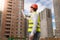 Male architect standing on building site and pointing on buildings under construction with blueprints