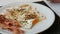 Male aristocrat eating morning scrambled fried eggs with bacon and red sauce on white plate with a knife and fork