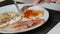 Male aristocrat eating morning scrambled fried eggs with bacon and red sauce on white plate with a knife and fork