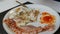 Male aristocrat eating morning scrambled fried eggs with bacon and red sauce on white plate with a knife and fork