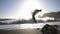 A male athlete doing a back somersault and landed on his feet on the beach, side view in slow motion. Nature summer