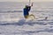 A male athlete engaged in snow kiting on the ice of a large snowy lake. He goes skiing in the snow.