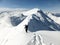 Male back country skier carrying his skis along a narrow snow ridge