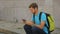 Male backpacker sitting on roadside, looking at his smartphone, tourist route