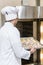 male baker in white chefs uniform putting baking tray with uncooked dough