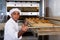 Male bakery worker pulls bread pan out of oven