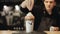 A male barista hand sprinkling confectionary dressing over milkshake with donut and whipped cream