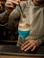 Male barman accurate holds piece of ice over steaming wine glass decorated with gold