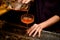 Male bartender pouring a alcoholic drink from the the one glass with ice cube to another