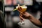 Male bartender serving yellow alcoholic cocktail in the glass with a dried lemon and leaf in the clothespin