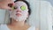 A male beautician makes a female client a vegetable therapy on her face in a spa salon