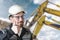 A male builder in a white hard hat against a blurred background of a construction site with a blue sky. Positive civil engineer