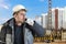 A male builder in a white hard hat against a blurred background of a construction site with a blue sky. Positive civil engineer