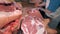 A male butcher is cutting skin and some pieces off the slab of meat