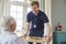 Male care worker serving dinner to a senior man at his home