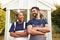 Male Carpenter With Female Apprentice Standing In Front Of Finished Outdoor Summerhouse In Garden