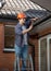 Male carpenter in red hardhat repairing house rooftop with hammer