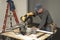 Male carpenter wearing tool belt and cutting wood board with professional chop saw on construction site home remodel