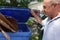 Male Caucasian senior citizen holding open the lid of a recycling trash can and smiling as he looks at the cardboard inside