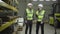 Male Caucasian worker in vest and helmet checking warehouse as his colleague coming up and shaking his hand. Metal plant