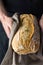 Male chef baker holds in hands in grey cotton towel freshly baked homemade loaf of bread. Authentic style. Lifestyle photo