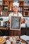 Male chef wearing a smiling apron holds a blackboard while standing