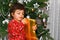 A male child unwrapping a golden wrapped gift with a Christmas tree at the back. Christmas holiday and gifts concept