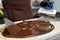 Male chocolatier uses a spatula to stir the tempered liquid chocolate on a granite table.