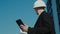 Male civil engineer contractor in safety helmet and jacket standing on construction site building and using mobile phone