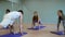 Male coach teaches women to stretch legs on blue mats
