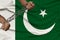 Male coarse hands chained in heavy iron chains against the background of the national flag of Pakistan, the concept of crime in