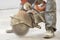 A male construction worker saws asphalt with a seamcutter, dust swirls from under the saw, construction and road work to repair