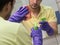 Male contractor from cleaning service i yellow t-shirt and violet rubber gloves holding a rag and spray and wiping the mirror