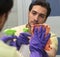 Male contractor from cleaning service i yellow t-shirt and violet rubber gloves holding a rag and spray and wiping the mirror