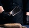 Male cook in black uniform and black latex gloves holds a large sharp meat knife over a cutting board