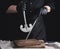 Male cook in black uniform and black latex gloves holds a large sharp vintage knife for meat and vegetables and a metal sharpener