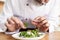 Male cook chef decorating garnishing prepared salad dish on the plate in restaurant commercial kitchen.