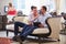 Male Couple Sitting In Hotel Lobby Looking At Digital Tablet