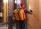 Male courier with thermo bag pushing intercom button. Food delivery