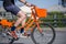 Male cyclist rides socially rented orange bicycle with basket on crossroad on city street