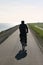 Male cyclist silhouette cycling on a dam pier with ocean on one side and green grass on the other. With copy space for writing