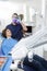 Male Dentist Examining Patient While Assistant Working At Dentis